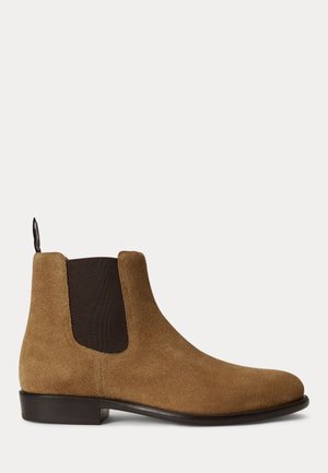 Bottine Chelsea en daim marron avec panneau latéral élastique noir, talon bas et languette de tirage sur fond clair uni.