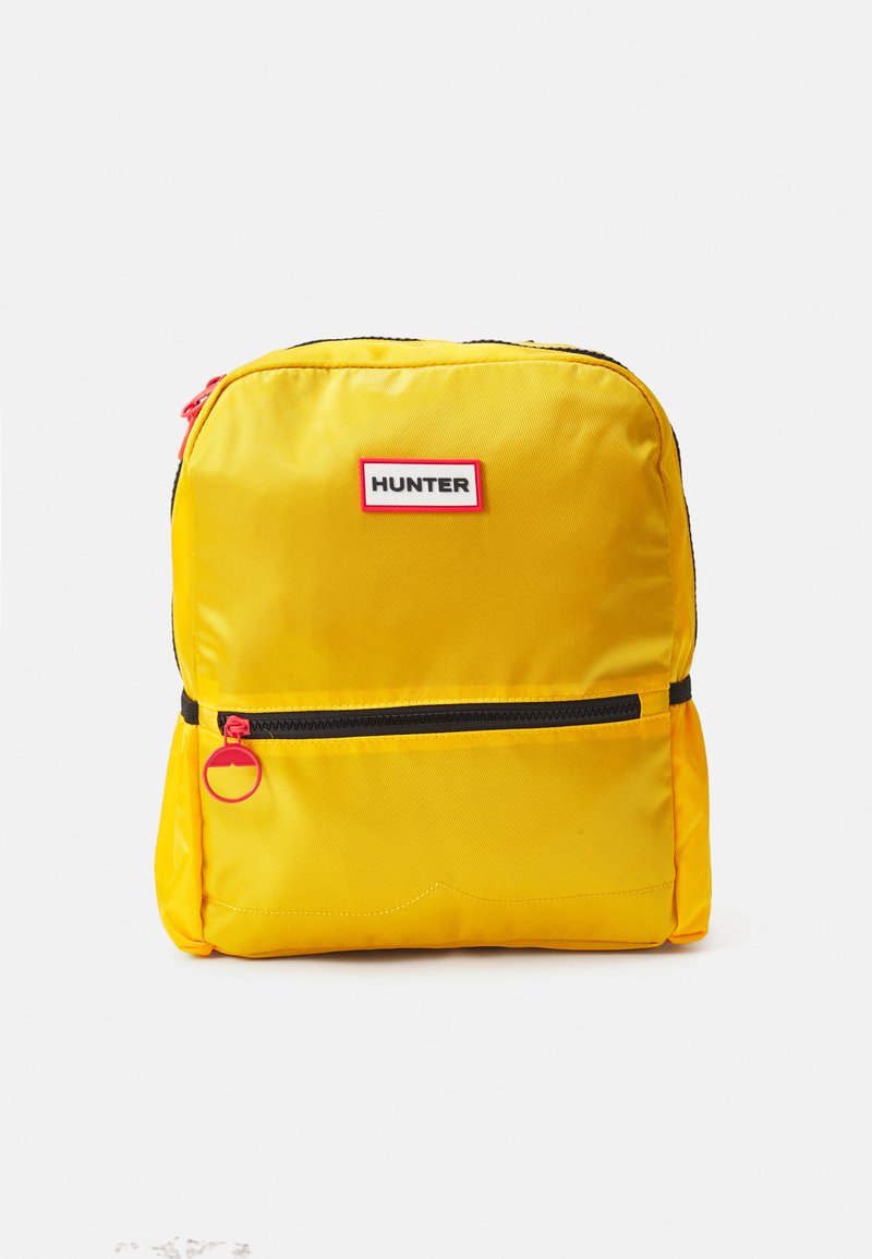 Mochila de nylon amarela com fechos pretos, um bolso frontal e uma etiqueta rotulada "HUNTER" em branco e vermelho. Apresenta um puxador de zipper redondo.