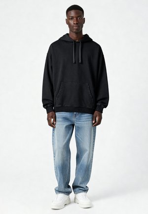 Sweatshirt noir à capuche avec une poche avant, associé à un jean bleu clair et des baskets blanches. Le tissu est doux avec une coupe décontractée.