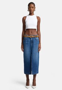 Crop top en tissu côtelé blanc associé à une longue jupe en denim bleu, doté d'une ceinture beige et de talons aiguilles blancs. Design simple et épuré.