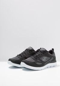 Black and grey athletic shoes with mesh upper, textured pattern, cushioned white sole, and lace-up design; features logo on the side.