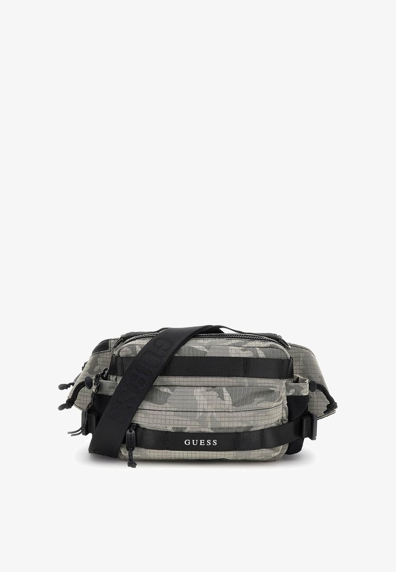 Sac bandoulière à motif camouflage en tissu texturé avec plusieurs compartiments zippés et une bandoulière noire réglable. Il arbore le logo 'GUESS'.