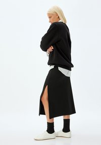 Zwarte lange rok met een zijsplit, gecombineerd met een zwarte sweatshirt, een wit shirt eronder en witte sneakers. Gladde stof structuur.