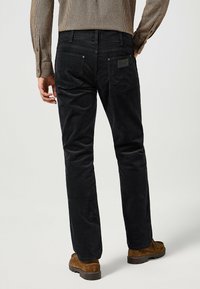 Zwarte corduroy broek met rechte pijpen, achterzakken met een ruitpatroon en een gestructureerde stofafwerking.