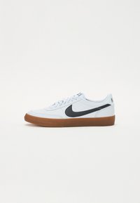 Ljust blå sneaker med svart Nike-logotyp. Har en texturerad gummisula och ett slätt ovandelmaterial, med vita snören och branding på hälen.