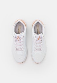 Bílé sportovní boty s hladkým svrškem, světle růžovými akcenty, perforovanými částmi pro prodyšnost a texturovanou gumovou podrážkou.