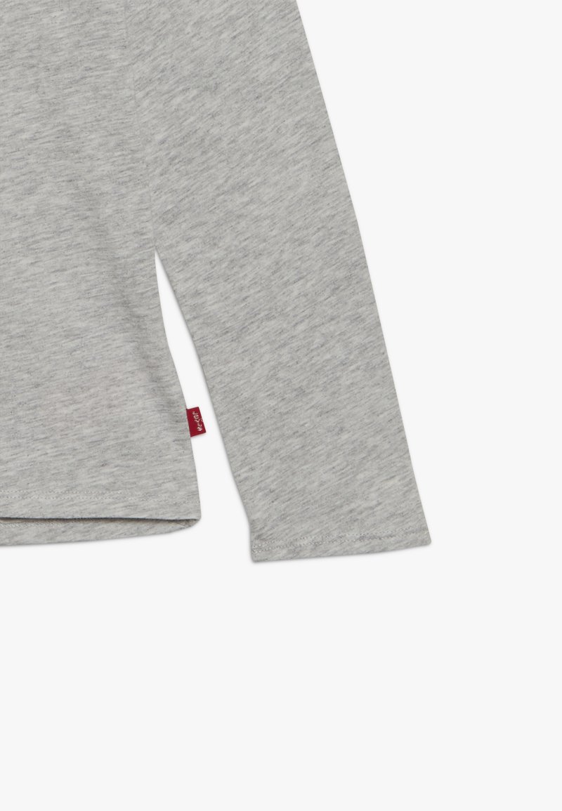 Camisa de manga larga gris hecha de una suave mezcla de algodón, con un corte recto y una pequeña etiqueta de la marca roja en el dobladillo.