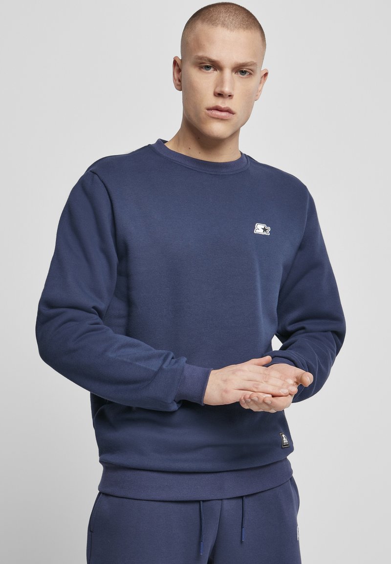 Mørkeblå sweatshirt lavet af en bomuldsblanding, med ribbede manchetter og nederkant, rund halsudskæring og et lille logo på brystet.