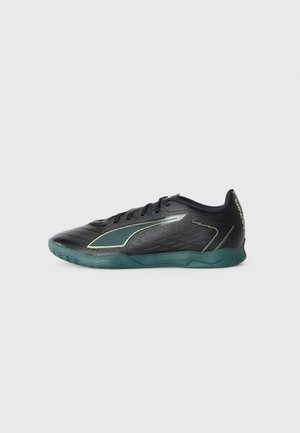 Black and dark green indoor soccer shoe with laces, textured upper, and "ULTRA" text on the heel, shown from the side on a white background.