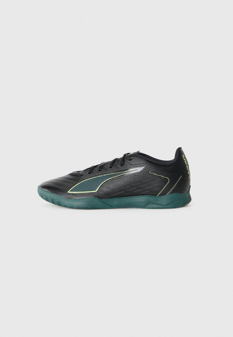 Scarpa da calcetto indoor nera e verde scuro con lacci, tomaia testurizzata e la scritta "ULTRA" sul tallone, mostrata di lato su uno sfondo bianco.