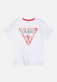 T-shirt en coton blanc avec un logo en triangle rouge portant le texte "GUESS®" et "WASHED JEANS", col rond et manches courtes.