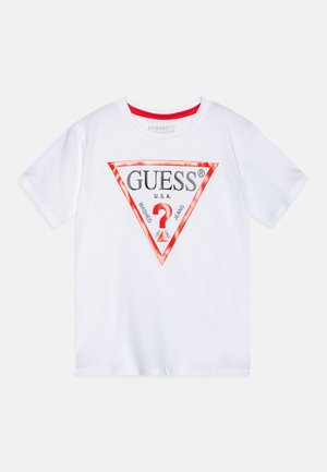 Bijela pamučna majica s crvenim trokutastim logotipom s natpisima "GUESS®" i "WASHED JEANS", okruglim izrezom i kratkim rukavima.