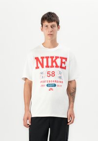 White cotton t-shirt with red and blue graphics, featuring "NIKE," "58," and "SKATEBOARDING" designs. Short sleeves, relaxed fit.