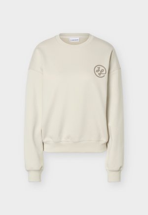 Cream-colored long-sleeve sweatshirt with ribbed cuffs and hem, crew neck, and small circular logo on the left chest.