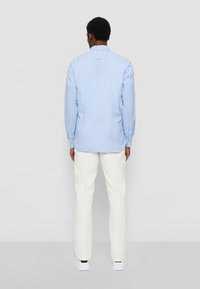 Camicia a maniche lunghe blu a scacchi in tessuto, con colletto abbottonato e pantaloni bianchi. La camicia ha una vestibilità comoda.