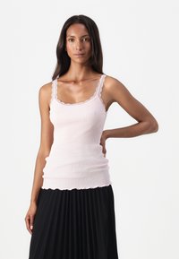 Top aderente rosa chiaro a costine con bordi e spalline scallop, caratterizzato da un design aderente. Il tessuto appare liscio con una leggera elasticità.