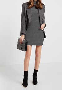 Valkoinen ja musta ruudullinen bleiseri mustavalkoisen raidallisen mekon päällä. Asua täydentää teksturoitu musta käsilaukku ja mustat nilkkurit.