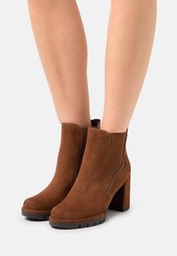 Stivaletti alla caviglia in pelle scamosciata marrone con tacco a blocco, dotati di pannelli elastici laterali e punta rotonda. Superficie testurizzata e suola resistente.