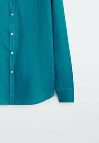 Turkosa knapp-up skjorta gjord av ett texturerat tyg, med rundad nederkant, långa ärmar och plastknappar längs knappslån.