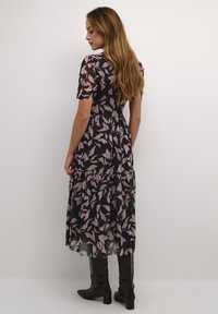 Abito maxi a fiori neri e rosa con maniche corte, gonna a strati e dettagli trasparenti; abbinato a stivali neri lucidi fino al ginocchio.