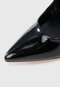 Pantof negru cu toc înalt din piele lacuită, cu vârf ascuțit și suprafață netedă, lucioasă; are un design cu partea superioară decupată.