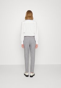 Witte overhemd met lange mouwen en een geplooide achterkant, met knoopmanchetten, gecombineerd met lichtgrijze, op maat gemaakte broek en off-white schoenen. Eenvoudig ontwerp.