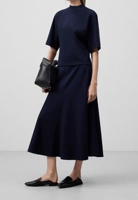 Robe bleu marine à manches courtes et col haut, fabriquée en tissu lisse. Complétée par un sac à main noir et des chaussures noires plates.