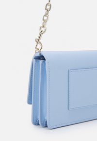 Borsa a tracolla in pelle azzurro chiaro con una texture liscia, dotata di una pattina, una tracolla a catena e una piccola tasca esterna.