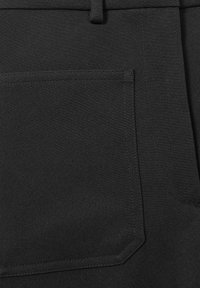 Primo piano di una tasca di pantaloni in tessuto nero con cuciture visibili e passante per cintura nella parte superiore.