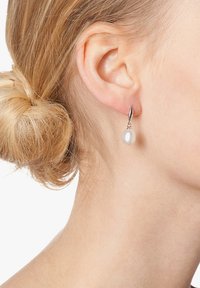 Náušnice striebornej farby s jednou bielou perlou visiace na elegantnom háčiku. Perly majú hladký, lesklý povrch.