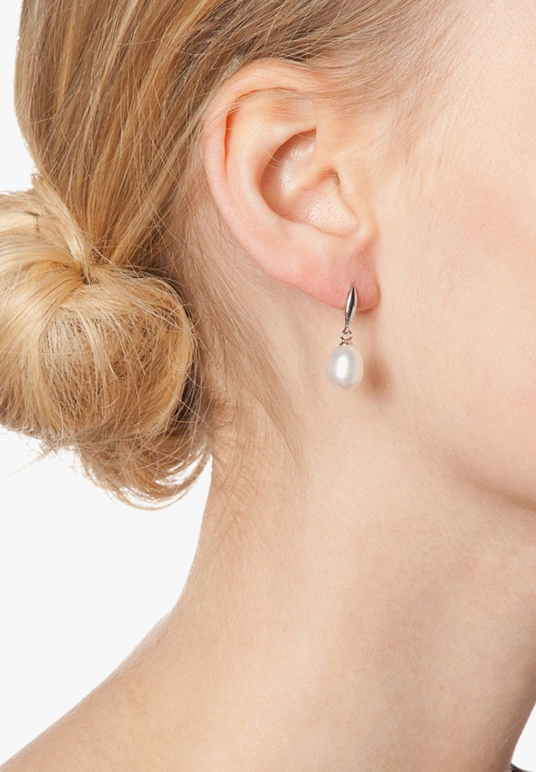 Náušnice striebornej farby s jednou bielou perlou visiace na elegantnom háčiku. Perly majú hladký, lesklý povrch.