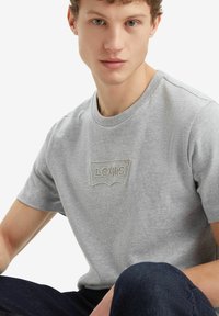 Camiseta de algodón gris con mangas cortas, que presenta un logotipo bordado de Levi's en la parte frontal y un escote redondo.