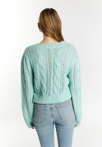 Mintgrön stickad tröja med kabelstickningsmönster, ribbad nederkant och öppenstickningsdetaljer, tillsammans med ljusblå jeans i en figursydd stil.
