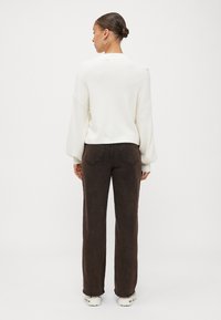 Weißer, strukturierter Pullover mit langen Ärmeln, kombiniert mit dunkelbraunen, hochgeschnittenen Jeans. Das Outfit zeichnet sich durch eine lockere Passform und minimale Details aus.