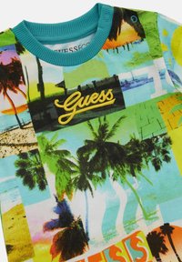 T-shirt z krótkim rękawem z żywym nadrukiem palm, plaż i zachodów słońca w kolorach zielonym, turkusowym i żółtym, z haftowanym logo "Guess".