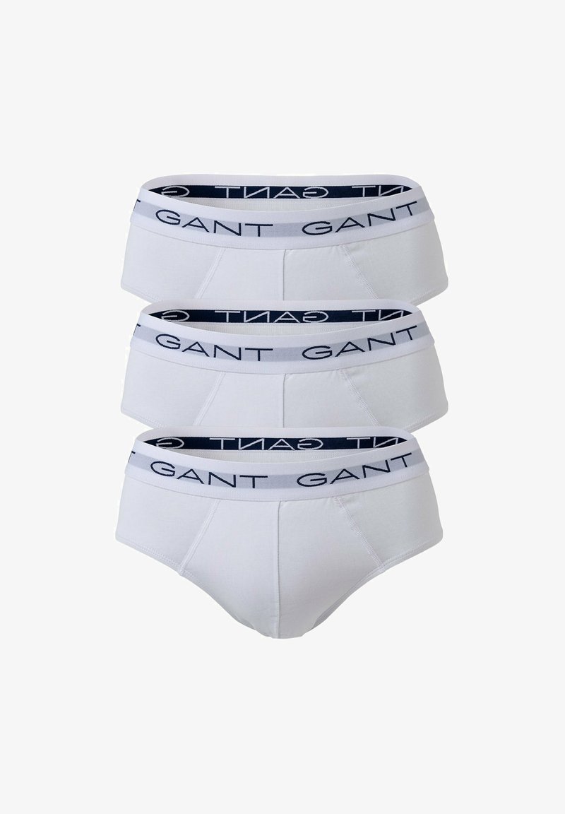 Trzy pary białych bawełnianych slipów z granatowym elastycznym paskiem w talii z nadrukiem "GANT" w kolorze białym. Klasyczny krój o gładkiej fakturze.