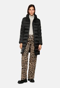 Schwarze Pufferjacke mit Kapuze und gestepptem Design. Kombiniert mit beigen, leopardgemusterten Schlaghosen und schwarzen klobigen Schuhen.