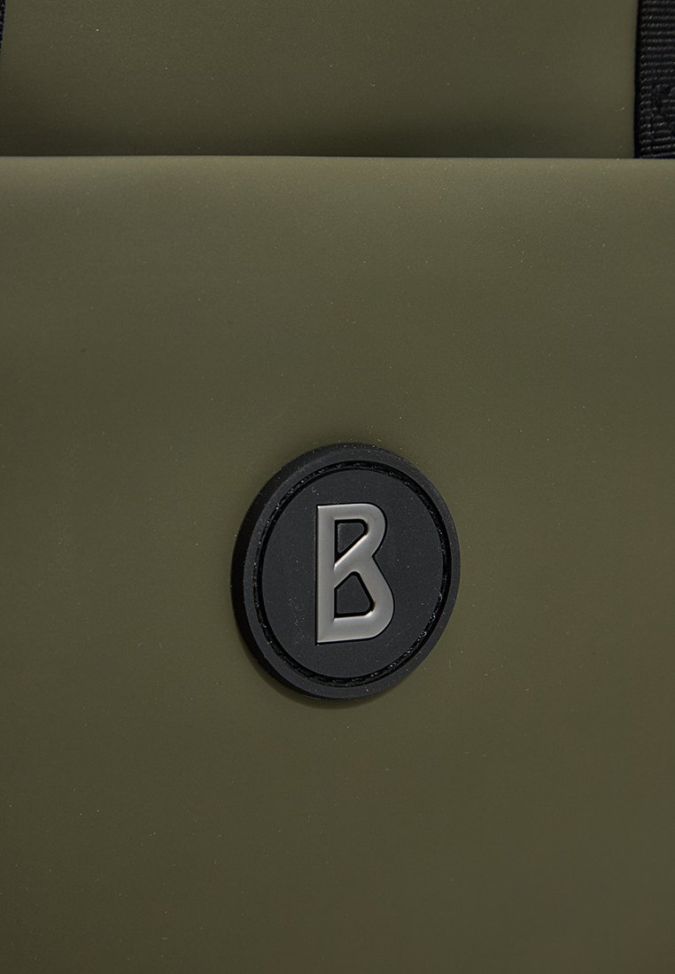 Olivgrüne Tasche mit einer strukturierten Oberfläche und einem runden schwarzen Logo mit dem silbernen Buchstaben "B". Schlichtes Design mit minimalen Details.