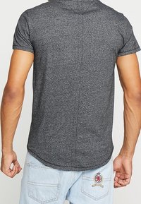 Gray short-sleeve shirt with a rounded hem, made from textured fabric. Features a subtle seam detail on the back. No visible logos or patterns.