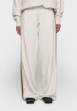 Pantaloni della tuta larghi color crema realizzati in tessuto morbido, con righe laterali, vita elastica e dettagli ricamati minimal.