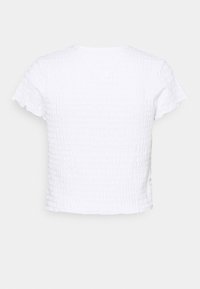 Vit kortärmad texturerad blus med ett rynkat mönster och lätt volangkant vid ärmar och fåll, visad bakifrån.