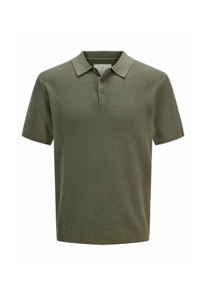 Garçon aux cheveux bouclés portant un polo en maille vert à manches courtes, un short beige jusqu'aux genoux, des chaussettes crème et des chaussures en cuir marron, debout face à l'avant.