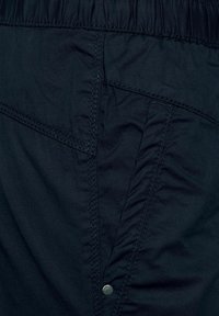 Marinblått tyg med subtil lyster; har resårmidja, lagerdesign och en metallknapp som detalj. Mjuk, lätt textur.