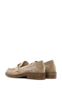 Mocasines de ante en beige claro con un tacón bajo y apilado, que presentan un distintivo adorno de cadena dorada a lo largo del empeine. Textura suave.
