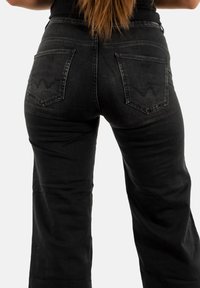 Jeans in denim nero con vita alta, gambe ampie e due tasche posteriori con un design ricamato. Il materiale è strutturato e leggermente sbiadito.