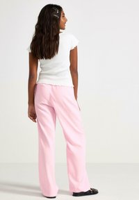 Witte geribbelde top met korte mouwen en roze losse broek met een geschulpte zoom. De outfit heeft een ontspannen pasvorm en een soepel textuur.