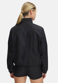 Giacca nera leggera con collo alto, polsini elastici e vestibilità comoda. Presenta una texture liscia e un design semplice.