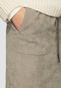 Beige corduroy rok met frontzakken en een elastische tailleband met trekkoord. Zichtbare textuur met een zachte, fluweelachtige uitstraling.