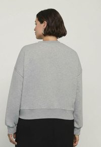 Felpa grigia corta con spalle basse, polsini e orlo a coste. Tessuto morbido in misto cotone con una trama liscia e design minimal.