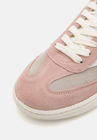 Rosa suedesneaker med lysegrå detaljer, hvite snørebånd og en teksturert såle. Buet design med utskjæringer nær tåen.